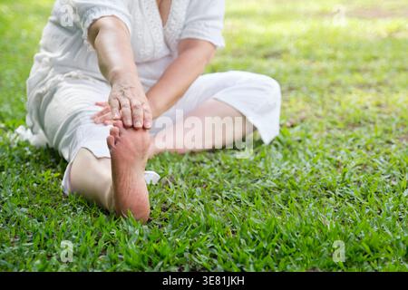 Immagine ritagliata di una donna anziana ispanica che fa esercizi di stretching seduta sull'erba nel parco durante il giorno Foto Stock