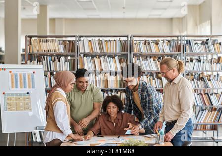 Gruppo di studenti che studiano insieme a un insegnante maschile in biblioteca Foto Stock