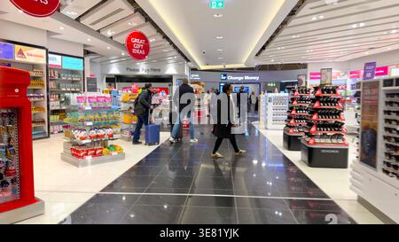 Gli amanti dello shopping con i bagagli camminano attraverso un negozio al dettaglio World Duty Free nel terminal dell'aeroporto di newcastle con mostre di regali e cambio valuta Foto Stock