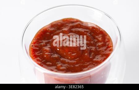 Salsa di pomodoro rosso fresco con erbe aromatiche in un recipiente di vetro trasparente, isolato su sfondo bianco. Foto Stock