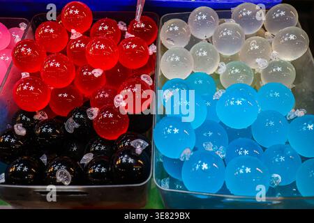 Palle di gelatina traslucide di colore rosso nero bianco e blu al mercato di strada tailandese, con vista dall'alto concetto di dessert che mostra colori vivaci e uno stile di vita giocoso. Foto Stock