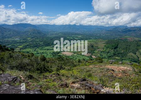 Vasto paesaggio caratterizzato da una valle verdeggiante con campi agricoli, circondato da colline ondulate e montagne lontane sotto un cielo azzurro nuvoloso, altissimo Foto Stock