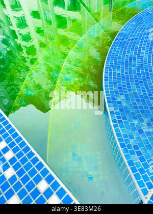 L'area della piscina ha piastrelle blu e acqua verde con riflessi dagli edifici circostanti visibili. La scena si svolge in un complesso residenziale Foto Stock
