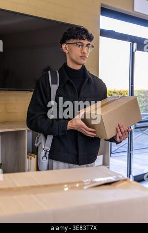 Uomo asiatico in piedi al ricevimento da una porta di vetro che tiene una scatola sigillata, una scatola con nastro sul bancone Foto Stock