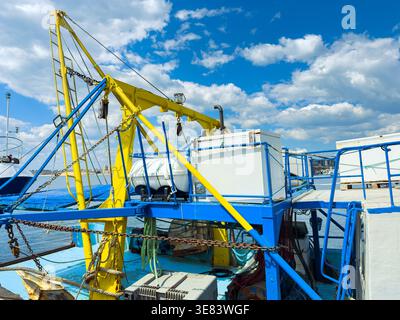 Una barca da pesca siede al molo. Sul ponte sono visibili attrezzature metalliche. Il cielo è per lo più limpido con alcune nuvole in alto. La scena mostra un lavoro Foto Stock