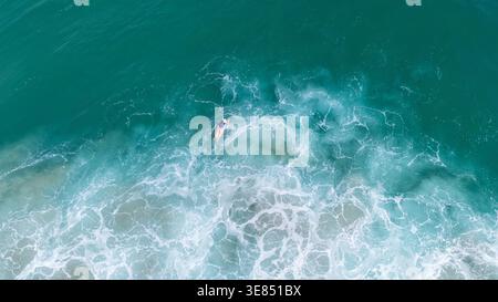 Vista aerea dall'alto verso il basso dei surfisti che pagaiano nelle acque turchesi dell'oceano con onde bianche e spumeggianti, sfondo marino minimo, avventura estiva e conc. Libertà Foto Stock