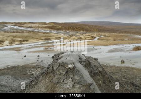 Un ampio colpo di un vulcano di fango con l'argilla grigia frizzante. La scena mostra un paesaggio arido e desolato con rigogliose acque e terre asciutte e incrinate Foto Stock