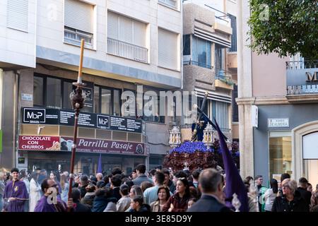 Almeria, Spagna - 30 marzo 2026: Un galleggiante raffigurante Gesù che trasporta la croce avanza attraverso una strada affollata durante una processione della settimana Santa nel cit Foto Stock