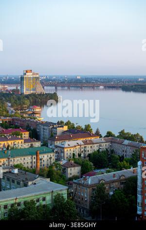 Dnipro, Ucraina – 19 maggio 2023: Un colpo ad angolo alto cattura il fiume Dnieper che scorre attraverso la città, con l'incompiuto Parus Hotel di colore giallo e blu Foto Stock
