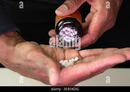 Un uomo nero che versa vitamine rotonde da una bottiglia nella mano sinistra nella mano destra Foto Stock