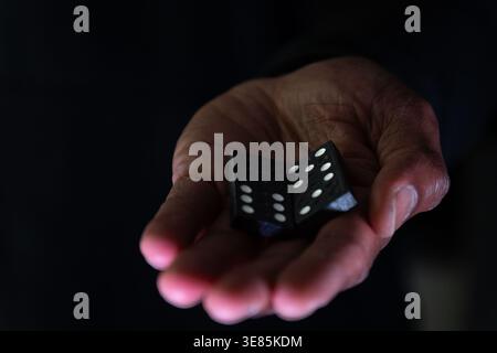 Due pezzi di domino con i numeri cinque, tre e sei su di loro in un palmo chiuso di una mano nera di mans Foto Stock