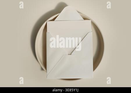 Busta quadrata minima e mockup su piastra, sfondo beige neutro, elegante modello di branding per cancelleria, ombre morbide. Invito a pulire la carta Foto Stock