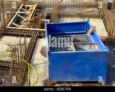 Primo piano di una fondazione in calcestruzzo in costruzione con gabbie per tondini in acciaio, casseforme e una cassetta di stoccaggio in metallo blu in loco, che mostra edifici e civili Foto Stock