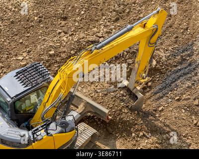 Vista dall'alto ad angolo elevato di un escavatore idraulico giallo che lavora in cantiere, scavo e spostamento di terreno e ghiaia in un'area di lavorazione del terreno con sgrossatura Foto Stock