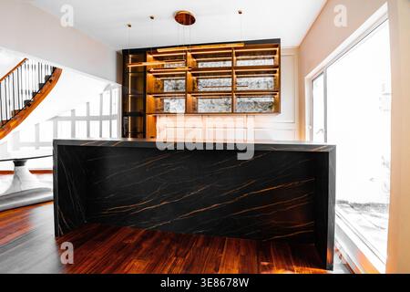 Interni lussuosi e minimalisti con un elegante bancone da bar in marmo nero, pavimento in legno caldo, scaffali in ottone e illuminazione soffusa in un ambiente moderno e arioso Foto Stock