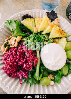 Primo piano di un piatto di insalata fresca con verdure miste, ananas grigliato, uva verde, anacardi, insalata di barbabietole tritate, e un formaggio morbido, servito per un Foto Stock
