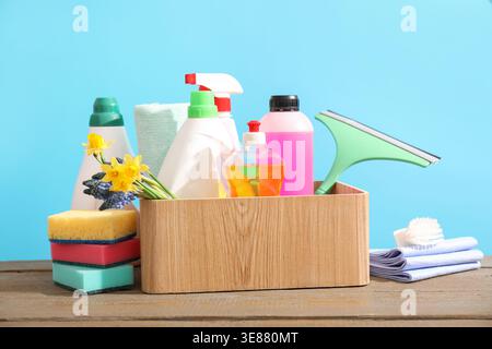 Pulizia di primavera. Detersivi, forniture e fiori su un tavolo di legno su sfondo azzurro Foto Stock