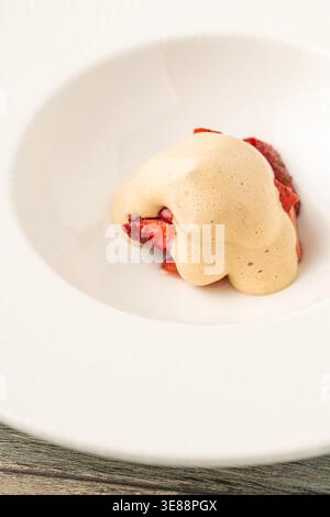 Dessert gourmet minimalista con frammenti di fragole sotto panna in un piatto elegante Foto Stock