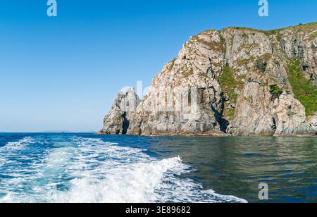 Le aspre scogliere di pietra si innalzano bruscamente dalle acque blu profonde dell'oceano sotto un cielo estivo limpido e luminoso Foto Stock
