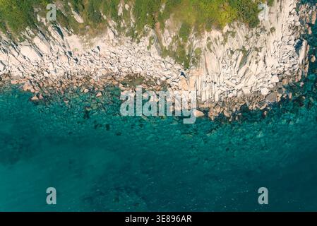 L'aspra costa rocciosa incontra le limpide acque turchesi dell'oceano, rivelando formazioni sottomarine e vegetazione verde da una vista aerea Foto Stock