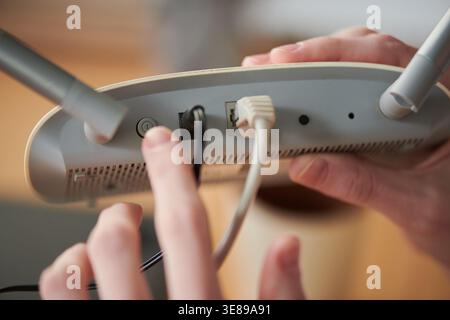 Primo piano di mani adulte che collegano i cavi al router wireless, premendo il pulsante di accensione per la configurazione Internet e l'installazione della rete domestica. Utile per la banda larga, il supporto tecnico e gli annunci di connettività Foto Stock