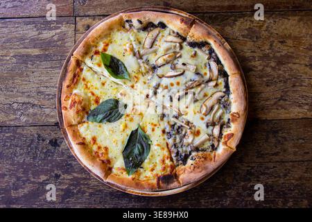 La pizza appena sfornata su un tavolo di legno è condita generosamente Foto Stock