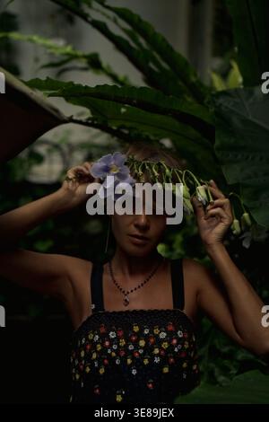 Donna seria che tiene fiori blu sopra la testa nella giungla, Bali Foto Stock