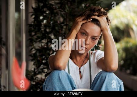 Giovane donna stressata seduta all'aperto con le mani che tengono la testa Foto Stock
