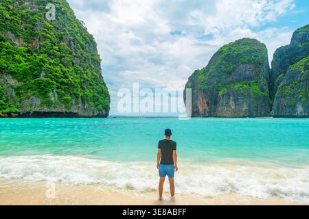 Uomo turistico in piedi sulla costa marina della spiaggia di sabbia tropicale Maya Bay con acque turchesi oceani e scogliere sulle isole Phi Phi, Krabi, Thailandia. Indietro Foto Stock