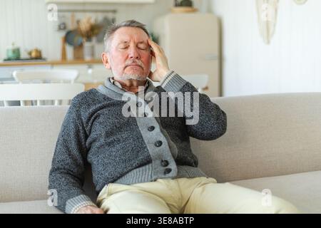 Mal di testa. Anziano infelice di mezza età che soffre di mal di testa malato che sfrega le tempie a casa. Vecchio nonno anziano maturo che tocca i templi che soffre di stress. Un uomo che sente dolore alla testa Foto Stock