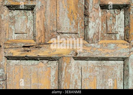 Vista ravvicinata della vecchia superficie della porta in legno angosciato che mostra strati di vernice sbucciata e motivi a grana di legno naturale Foto Stock