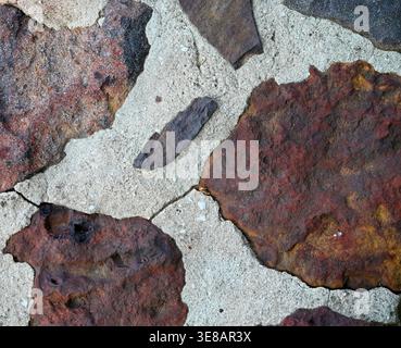 Vista ravvicinata della superficie in pietra mista con pietre rosse arancioni e grigie, consistenza porosa ruvida, Malta bianca con crepe e polvere sparsa Foto Stock