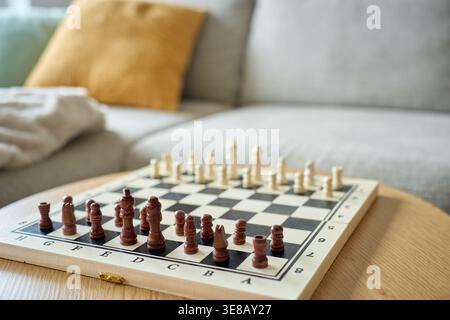 Scacchiera in legno con pezzi disposti sul tavolo pronti per giocare nell'interno del soggiorno. Concetto di strategia, logica, attività ricreative e gioco intellettuale. Foto Stock