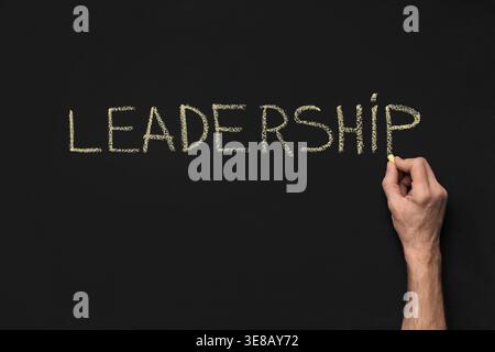Scrittura lavagna di Leadership con gesso di tenuta manuale su sfondo nero Foto Stock