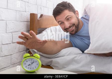 Uomo felice che si sveglia e ferma la sveglia Foto Stock