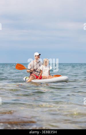 Padre e figlia condividono momenti speciali in paddleboard in mare in una giornata di sole, godendosi il tempo trascorso in famiglia e divertendosi all'aria aperta. Foto Stock