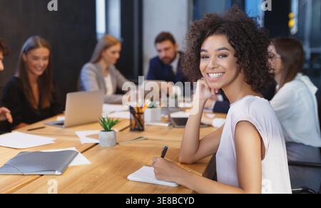 Giovane imprenditrice sorridente in telecamera alla riunione Foto Stock
