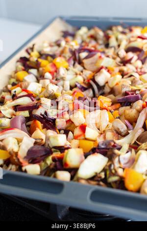 Le verdure fresche vengono tritate e poste su una teglia da forno pronta per la cottura in forno. Vengono presentati ingredienti colorati e l'ambiente e' una cucina accogliente Foto Stock
