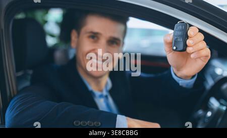 Man sorride e tiene le chiavi dell'auto vicino a un veicolo presso una concessionaria nel pomeriggio Foto Stock