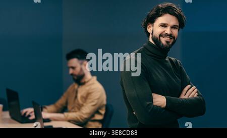 Gruppo di persone che lavorano in ufficio con una persona sorridente alla fotocamera mentre un'altra lo digita Foto Stock