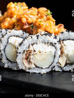 Panini di sushi con semi di sesamo e ripieni cremosi. Condita con vivace insalata di gamberi arancioni. La piastra scura in ardesia migliora il contrasto visivo. Fresco, appetizi Foto Stock