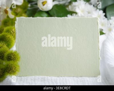 Biglietto da visita verde vuoto su tessuto di muschio bianco. Verde e sfondo bianco con fiori sfocati. Invito, annuncio, volantino, messaggio Foto Stock