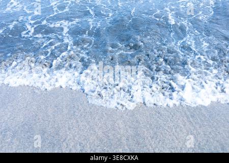 Onde oceaniche azzurre limpide che scivolano delicatamente sulla spiaggia di sabbia bianca del Giappone, acqua traslucida che cattura luce calda. Un paesaggio marino pulito e minimalista che evoca la pace, l'estate e la calma ritmica della natura in riva al mare. Foto Stock