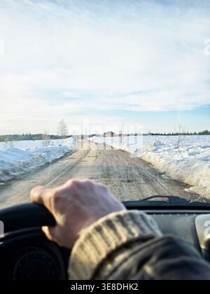 Il conducente vede davanti a sé una strada sporca, mentre la neve copre il terreno su entrambi i lati. Il viaggio continua su un percorso aperto. Foto Stock
