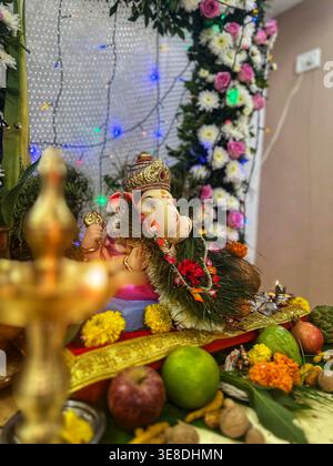 Idolo Ganesh decorato con tradizionale allestimento Puja. Immagine verticale ravvicinata di un idolo Lord Ganesha coronato e impreziosito da fiori freschi. Foto Stock