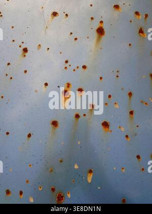 Una vista dettagliata dell'ossidazione su un pannello di metallo azzurro, caratterizzato da numerose piccole macchie di ruggine arancione-marrone e segni di gocciolamento verticali da Weather expo Foto Stock