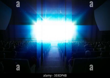 Un grande pubblico è seduto in un teatro, affascinato da un luminoso spettacolo sul palco. L'atmosfera e' piena di anticipazioni durante un regalo serale Foto Stock