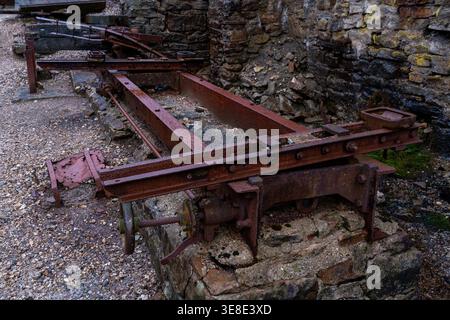Vista ravvicinata dei macchinari in ferro arrugginito e delle guide metalliche posizionate contro le pareti in pietra del vecchio mulino abbandonato Foto Stock
