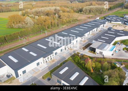 Vista aerea dei moderni edifici industriali in contrasto con le sfumature morbide degli alberi circostanti, Oostkamp, Fiandre, Belgio. Foto Stock