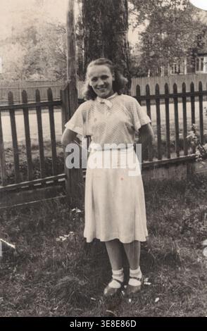 Giovane donna sorridente in camicetta bianca all'aperto vicino a Tree 1950s Foto Stock
